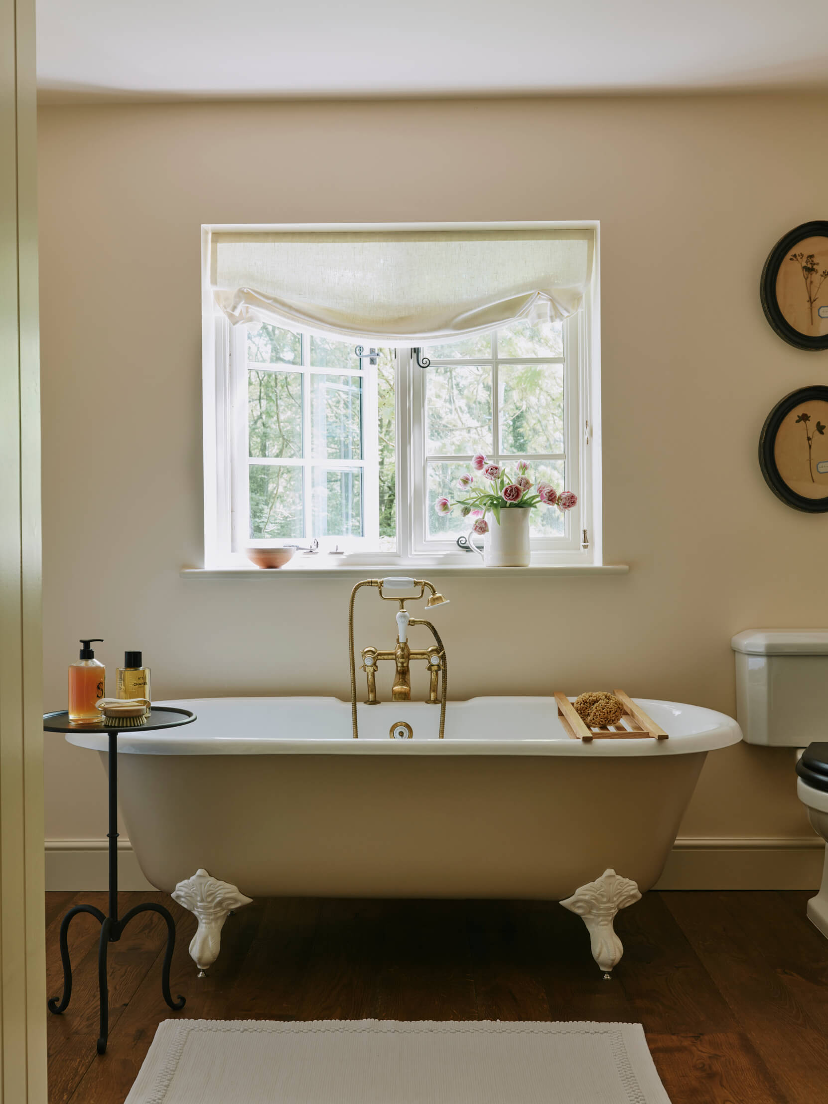 Dusty pink roll top bath underneath a window with a white linen blind. The floors are dark wood and the walls a setting plaster pink. Interior design by Studio Squire