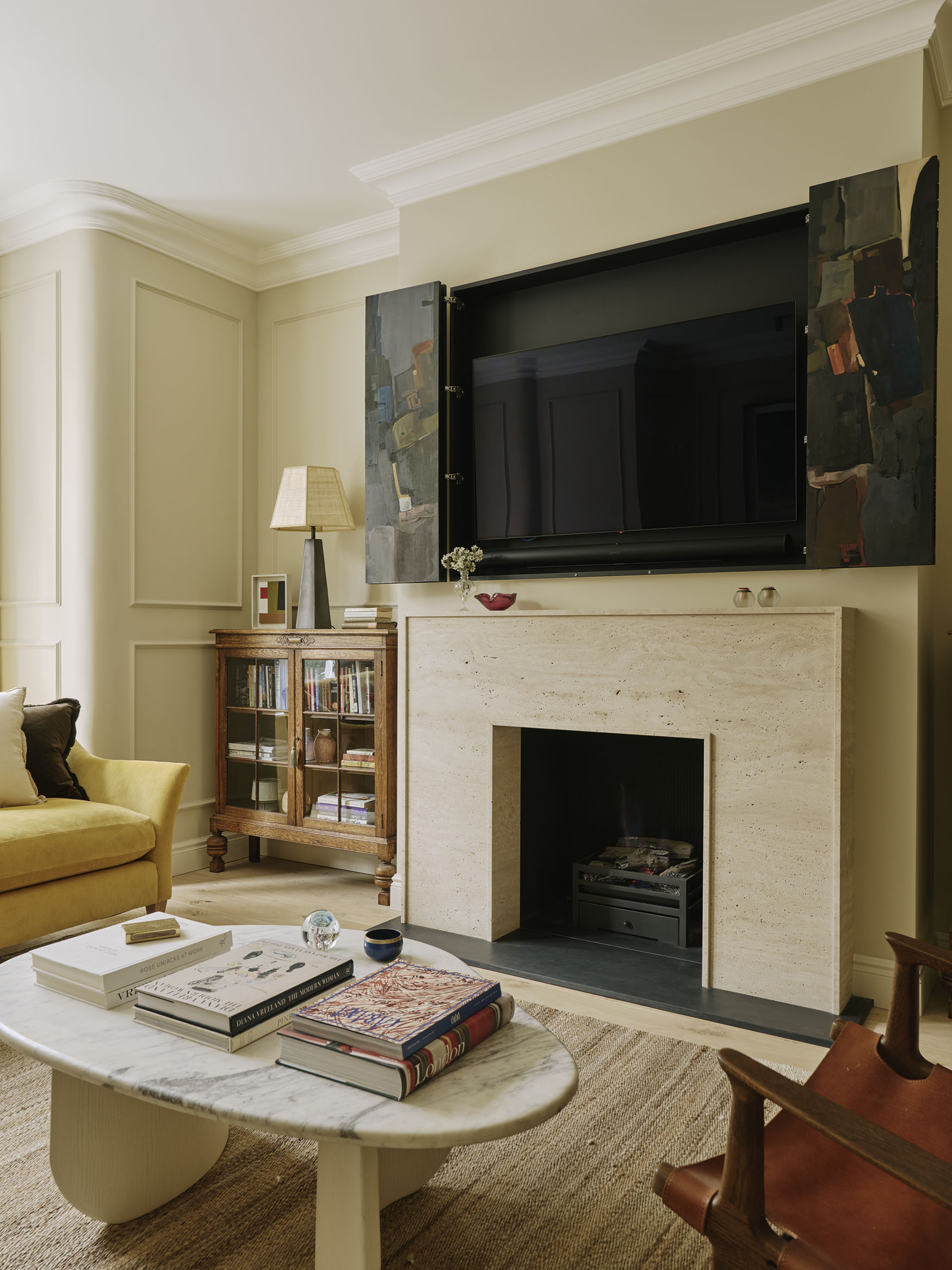 Painting above a fireplace opens up to reveal a TV underneath, interior design by Studio Squire